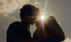 a man and woman kissing in front of the sun