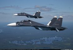 two fighter jets flying side by side in the sky above land and water below them