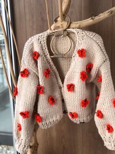 a knitted sweater with red flowers hanging from a hook