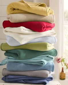 a stack of folded towels sitting on top of a window sill next to a vase with flowers