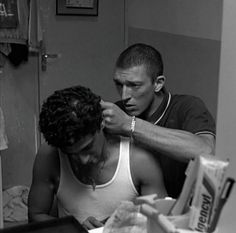 a man is brushing his hair in front of a mirror while another man looks on