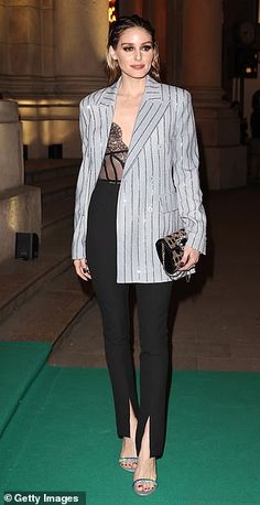 a woman standing in front of a building wearing a suit and holding a handbag