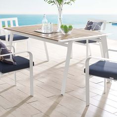 an outdoor table with two chairs and a vase on the table next to the water