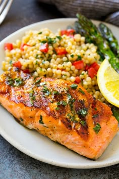 a white plate topped with salmon, corn and asparagus next to a lemon wedge