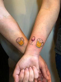 two people are holding hands with tattoos on their arms and one has a glass of wine