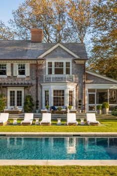 a large house with a pool in front of it and lawn chairs around the pool