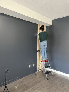 a woman standing on a stepladder painting the walls in a room with gray walls