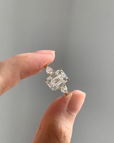 a woman's hand holding an engagement ring with two diamonds on it and the other side