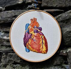 a cross stitch heart is hanging on a stone wall