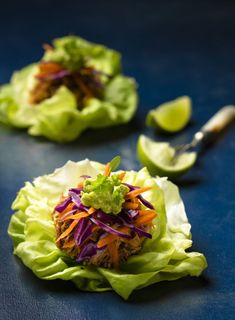 two lettuce wraps with shredded carrots and green onions on them, sitting on a blue surface