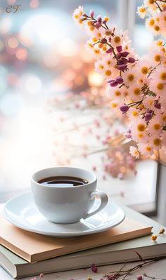 a cup of coffee sitting on top of a book next to a vase with flowers