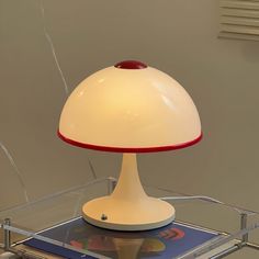 a white table lamp sitting on top of a glass shelf next to a cell phone