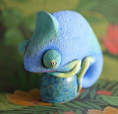 a blue and green toy animal sitting on top of a flowery surface with lots of water droplets