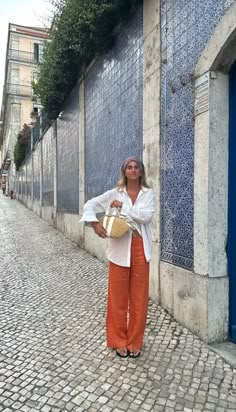 a woman standing in front of a building holding a basket and looking at the camera