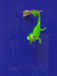 a green gecko hanging from a wooden branch on a blue wall with other items in the background