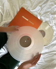 a person holding a white record in their hand and an orange book on the bed