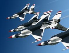 four jets are flying in the blue sky with white and red stripes on their wings