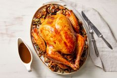 a roasted turkey on a platter with stuffing and gravy next to silverware