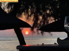 the sun is setting over the ocean with umbrellas