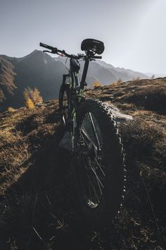 a mountain bike parked on top of a grass covered hill with mountains in the background