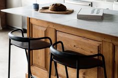 two black chairs sitting on top of a kitchen counter next to a book and cup