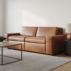 a brown leather couch sitting on top of a wooden floor next to a table and lamp