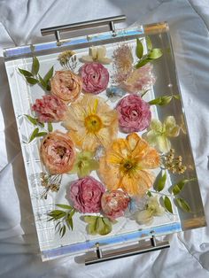 a glass tray with flowers in it on a white sheet