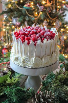 a cake with white frosting and raspberries on top sitting in front of a christmas tree