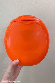 a hand holding an orange frisbee in front of a white wall and ceiling