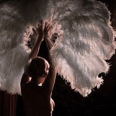 a woman with white feathers on her body holding up a large feathered object in front of her face