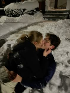 two people sitting in the snow hugging each other with their faces close to one another