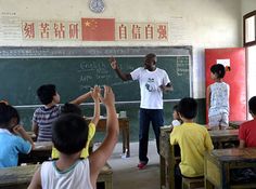 a group of children sitting at desks in front of a blackboard with writing on it