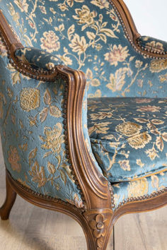 an ornate chair with blue and gold floral upholstering on the armrests