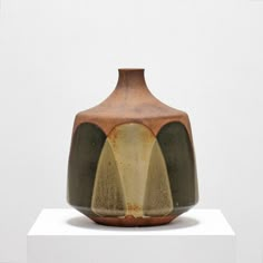 a brown and green vase sitting on top of a white pedestal in front of a wall