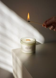 a person lighting a candle on top of a white table with the light coming from behind it