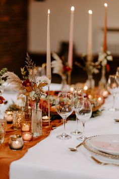 the table is set with candles, plates and wine glasses for dinner guests to enjoy