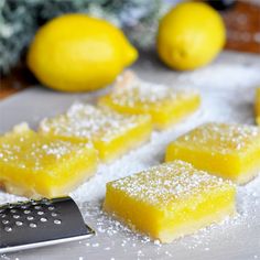 lemon pie bars on a cutting board with powdered sugar next to them and two lemons in the background