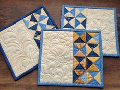 three blue and yellow quilted coasters sitting on top of a wooden table