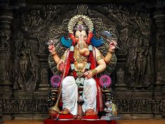 a statue of the god ganesh sitting on a throne in front of a wall