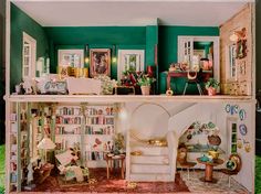 a doll house with furniture and bookshelves on the top floor, in front of a green wall