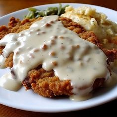 a white plate topped with fried chicken covered in gravy and mashed potatoes