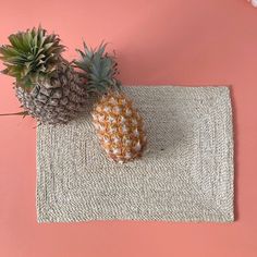 two pineapples sitting on top of a placemat next to each other in front of a pink wall