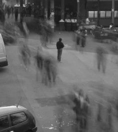 black and white photograph of people walking down the street in front of buildings with cars