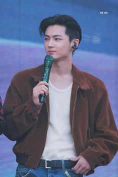 the young man is holding a microphone in his right hand and wearing a brown jacket