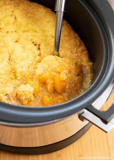 a crock pot filled with food on top of a wooden table next to a knife