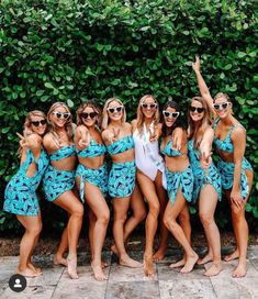 a group of women in matching blue swimsuits posing for a photo with bushes behind them