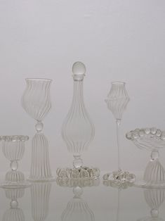 an assortment of glass vases sitting on top of a reflective surface in front of a white wall