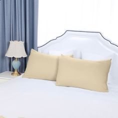 a white bed topped with two pillows next to a lamp