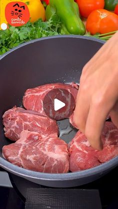 someone is cooking raw meat in a pan on the stove top with vegetables and peppers