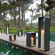 some candles are sitting on the edge of a pool in front of trees and water